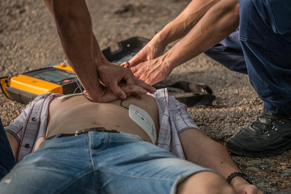A person performing CPR on an individual lying on the ground with an AED device nearby.